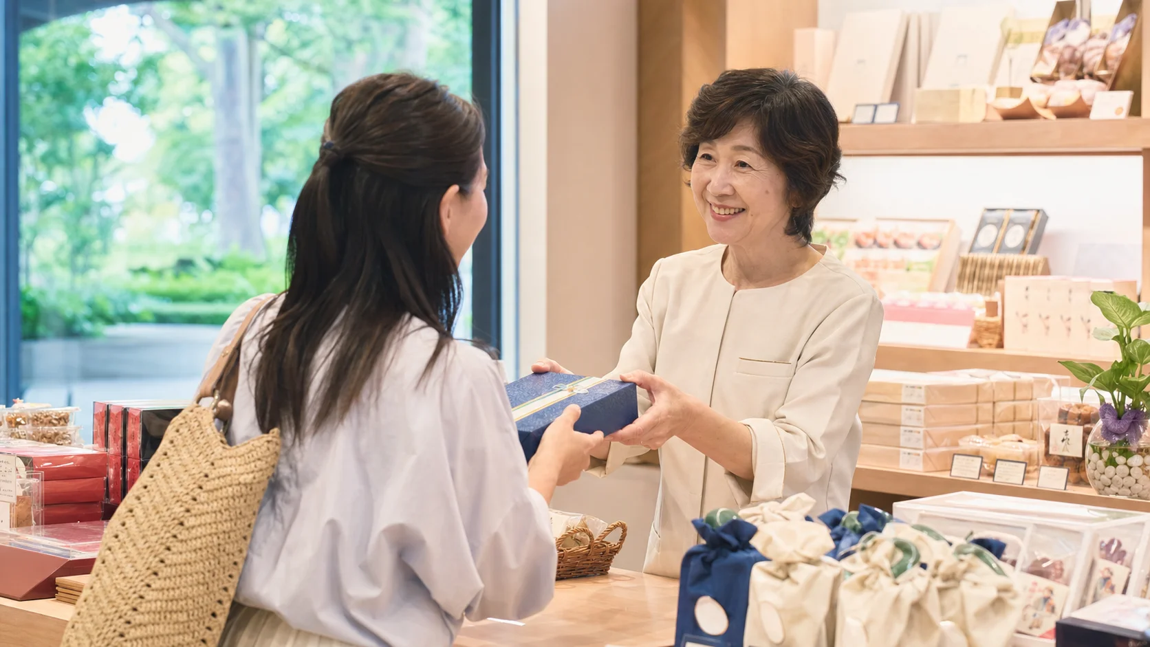 リゾートホテルの売店カウンターでお土産を手に取るお客さまに笑顔で対応するシニアスタッフ。明るく清潔な店内