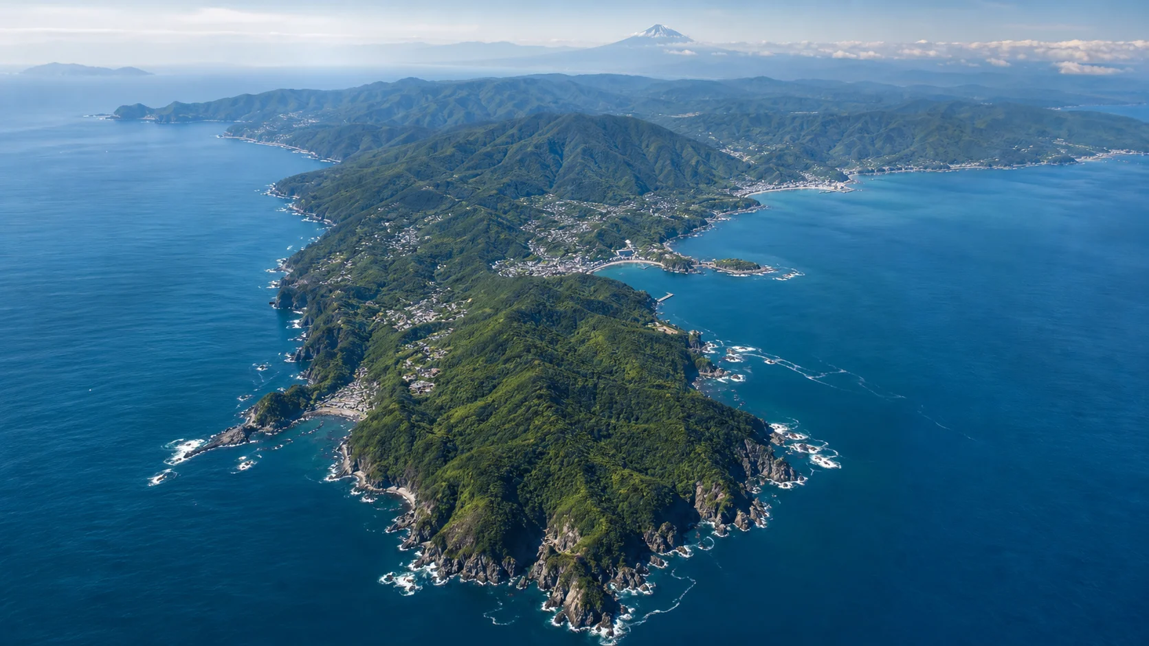 伊豆半島の海岸線と温泉地を望む穏やかな俯瞰の風景。緑の山々と青い海が入り組む半島の地形