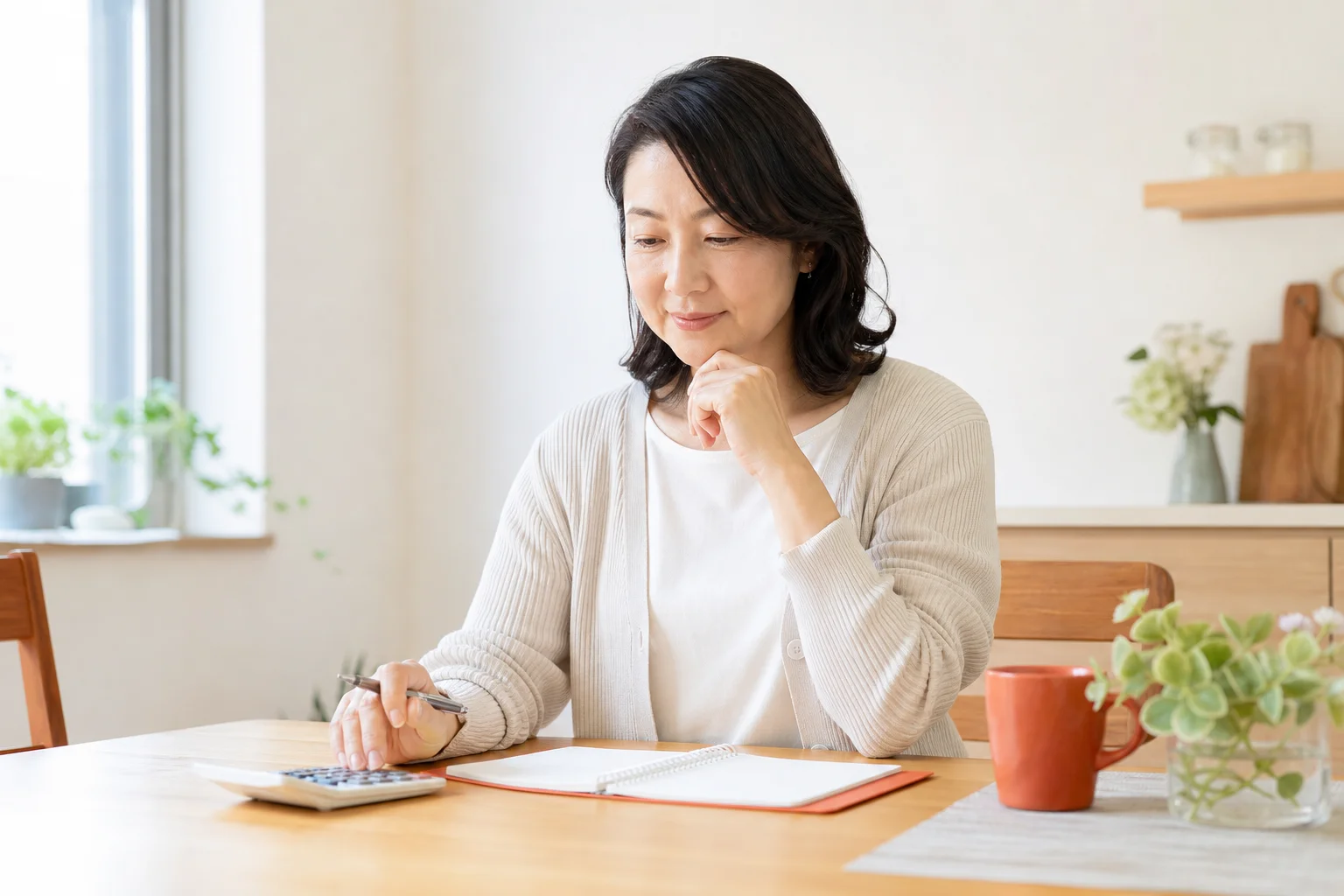 テーブルで家計の計算をしながら考え込む50代の様子