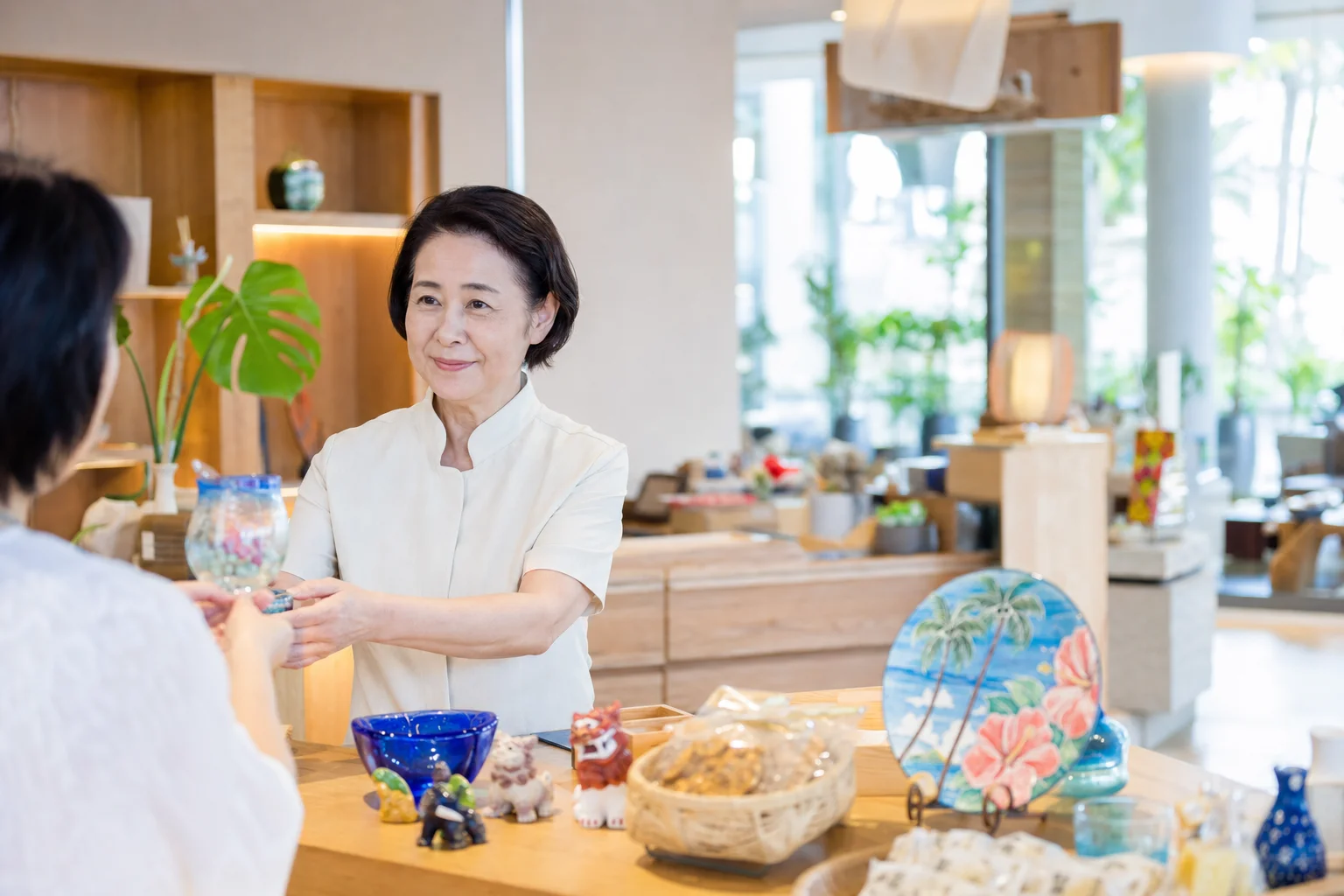 沖縄のリゾートホテルの売店カウンターでシニアスタッフが笑顔で接客している館内の様子